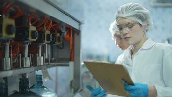 scientist worker checking the quality of water bottles on the machine conveyor line at the industrial factory. Female worker recording data at the beverages manufacturing line video