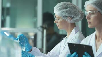 scientist worker checking the quality of water bottles on the machine conveyor line at the industrial factory. Female worker recording data at the beverages manufacturing line production. video