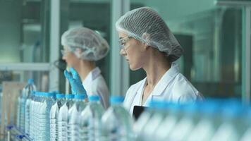 scientist worker checking the quality of water bottles on the machine conveyor line at the industrial factory. Female worker recording data at the beverages manufacturing line production. video