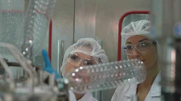 fábrica mujer ingeniero inspeccionando agua dispensador en el máquina. el trabajador cheques el calidad de agua botellas en el máquina transportador línea a el industrial fábrica. video