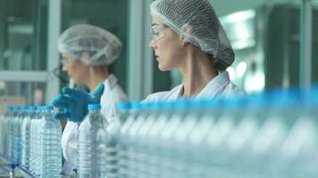 scientist worker checking the quality of water bottles on the machine conveyor line at the industrial factory. Female worker recording data at the beverages manufacturing line production. video