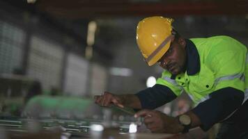 africano trabalhadores. engenheiro técnico segurando Smartphone para verificação e inspecionando às armazém fábrica. capataz reparação uma parte do máquina para pesado industrial. video