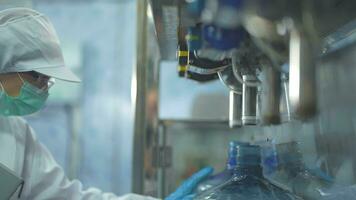 scientist worker checking the quality of water bottles on the machine conveyor line at the industrial factory. Female worker recording data at the beverages manufacturing line video