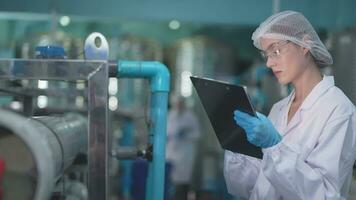 scienziato donna lavoratore controllo e monitoraggio il controllo pannello su macchina sistema a il industriale fabbrica. femmina lavoratore registrazione dati a il controllo pannello con misurare pressione di acqua livello. video