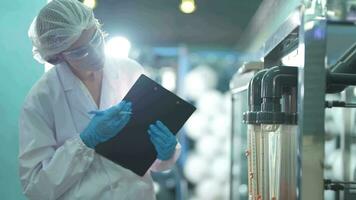 científico mujer trabajador comprobación y supervisión el controlar panel en máquina sistema a el industrial fábrica. hembra trabajador grabación datos a el controlar panel con medida presión de agua nivel. video