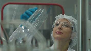 fábrica mujer ingeniero inspeccionando agua dispensador en el máquina. el trabajador cheques el calidad de agua botellas en el máquina transportador línea a el industrial fábrica. video