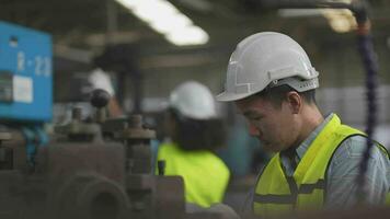 trabajadores fábrica asiático hombre trabajando a pesado máquina. grupo de personas operando en frente de motor fabricado a industrial planta fábrica. inteligente industria trabajador operando. mujer sonriente y contento. video