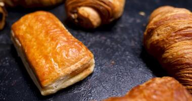 bladerdeeg gebakje, croissants en chocola gevulde deeg. onthullend een mengen van vers gebakje Aan een zwart achtergrond. video