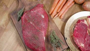 Panning over two pieces of grill ready meat. Top view of beef meat and raw vegetables video