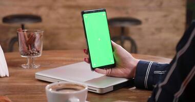 Slide shot from right to left of a womans hand holding a green screen smartphone. Looking at her smartphone. Watching video, reading text. video