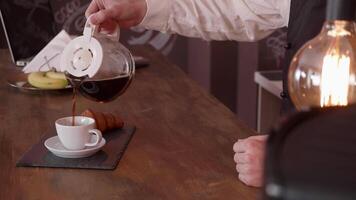 Cool cinemagraph of a mans hand pour coffee from a pitcher on a bar counter. Wooden bar counter and a bulb of pretty light. Best coffee. video