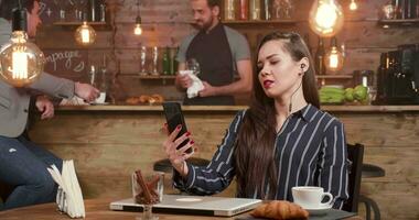 jong zakenvrouw nemen een video telefoontje in een koffie winkel. pratend Bij haar smartphone met een bedrijf partner of een vriend.