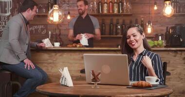 Cute woman using her headphones to talk in a restaurant. Having a conversation with a friend while serving a coffee. Laughing while socializing in a coffee shop. video