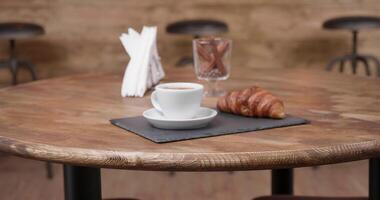 Slowly moving towards a restaurant table with an espresso and croissant on it. Minimalist composition in a wooden vintage style coffee shop. video