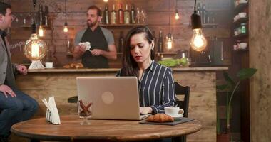jung, schön Frau konzentriert Schreiben ein Text beim ihr Laptop Arbeiten von ein Restaurant. Arbeiten jung Frau im ein hübsch, Jahrgang Kaffee Geschäft. video
