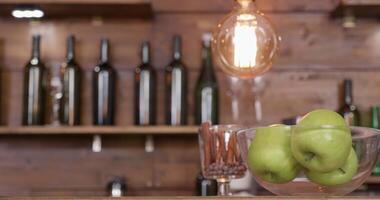 Slide movement from right to left revealing a bowl of apples a croisant and a white cup of black coffee. On a bar counter with bottles in a blured backgound. video