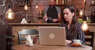 Female freelancer at a table in coffee shop waits for her colleague at a lunch break. A man aproaches and sits at the table close to her and starts a conversation. video