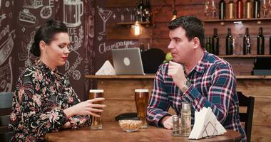 Beautiful couple drinking beer in vintage pub, restaurant. A bearded bartender is working at the counter in the background video