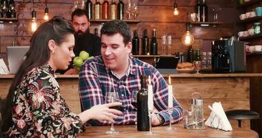 casal gastos uma romântico tarde dentro vintage bar ou restaurante. elas estão bebendo uma garrafa do vinho e ter velas em a mesa. uma barbudo hipster barman é dentro a costas trabalhando video