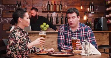 Eating pizza and drinking beer in a vintage rustic pub or restaurant. A bearded bartender is working in the background at the counter video