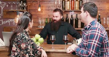 Couple drinking wine at the bar counter and talking with a bearded hipster bartender. They are in a vintage pub video