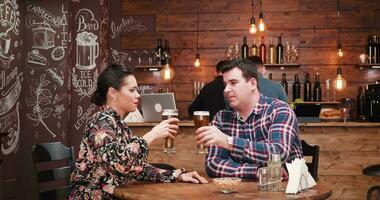 Couple being served with a pizza in vintage pub or restaurant by a bearded hipster waiter. There is another person drinking at the counter. video