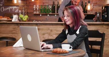 Woman types on laptop in vintage pub or coffee shop while an young bartender is working behind the counter video
