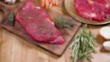 Revealing, handheld shot of a beef fillet on an aged board. Focused on a piece of raw meat. Blured composition of raw meat fillets and vegetables. video