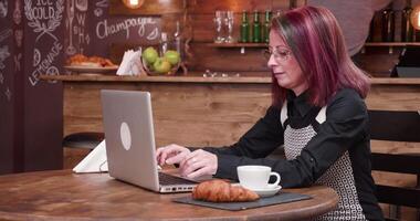 vrouw drankjes koffie terwijl typen Aan laptop toetsenbord in wijnoogst en elegant koffie winkel of kroeg video