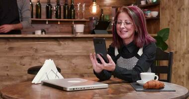 adulto mujer de negocios en un vídeo llamada mientras Bebiendo café en Clásico y estilizado pub, café tienda o restaurante video