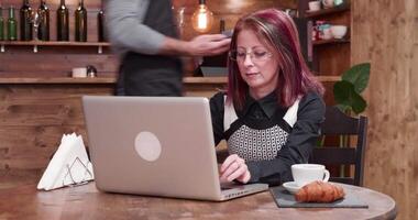 adulto mujer paga con nfc pagos en un Clásico café tienda mientras trabajando en su computadora video