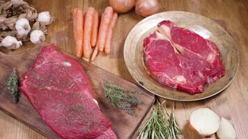 Sliding over a raw ribeye steak and a chunk of raw beef meat. Top view of fresh red meat on a wooden vintage background. video