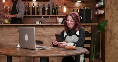 Zoomen im Schuss auf Erwachsene Geschäftsfrau im Video Anruf während Trinken ein Tasse von Kaffee im Jahrgang und gestylt Kaffee Geschäft