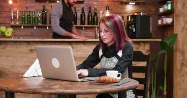 Zoom in shot on mature businesswoman in her 40s working on laptop in vintage and stylish coffee shop, pub or restaurant video