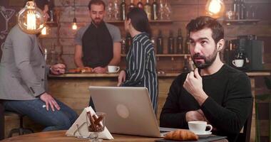 A man having an online call at his laptop while working in a coffee shop. Using his headphones to have a business conversation. video