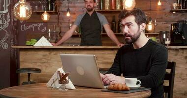 Young freelancer works and reacts as new costumers come in the cafe. Handsome caucasian bearded man distracted from his work while in coffee. video