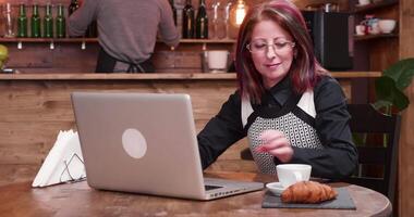 Adult businesswoman pays for coffee using a contactless credit card. She is working on the computer in a vintage coffee shop video