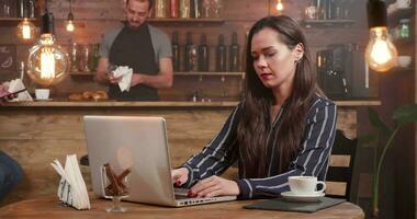 joven creativo mujer cierra su ordenador portátil y dejando el mesa de un pequeño café tienda. después un pequeño café descanso un bonito mujer en paz el restaurante. video