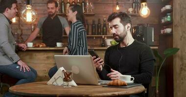 jong freelancer beantwoorden een telefoontje Bij zijn smartphone en sluit zijn laptop. afgelegen werk in een vriendelijk koffie winkel. video