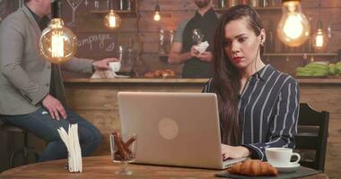 Young female freelance writer composing a text at her laptop. Medium shot on a slider. Cozy and pleasant atmosphere in a restaurant or bar. video