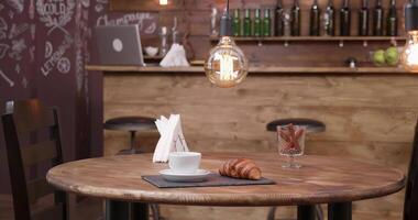 minimalistisk sammansättning av en kopp av kaffe och en croissant på en mörk bricka. parallax skott av en tabell för två i en skön tömma restaurang. video