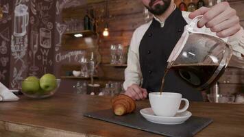 barista homme cinémagraphe tandis que il détient une lanceur de Frais brassée café et verse dans une vide Coupe. élégant, élégant, barbu barista remplissage une tasse de café. video