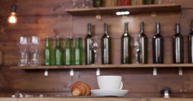 Parallaxe Schuss von ein Kaffee Tasse platziert auf ein Bar Schalter. dynamisch Hintergrund von verwischt Flaschen und Brille. video