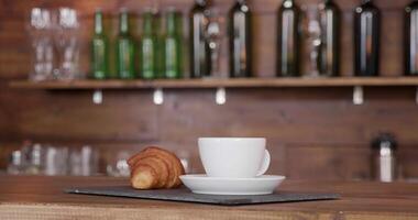 Close up shot of a croissant on the same tray with a cup of coffee. Bar style background in a cozy coffee shop. video