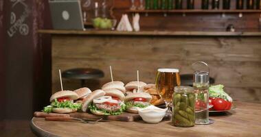 A wooden table with burgers on wooden boards in front of a bar. Beautiful composition of fresh burgers prepared for a burger party. video