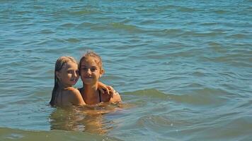 twee kinderen meisjes zwemmen in de zee en houding voor de camera, knuffelen. gelukkig jeugd. twee meisjes, zusters, zijn resting Aan de zee, zwemmen. video