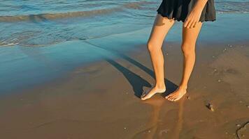 View of female legs walking on the beach in the water. Water splashes and foam from the waves washing the woman's legs in motion. Walks on the seashore video