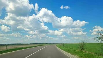 Vehicle point-of-view A view of the road while traveling by car. Green fields and blue sky with clouds. Beautiful nature of the flat landscape. video