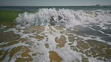 Top view of a sea wave arriving at a sandy beach in slow motion. Sea water foaming from hitting a sandy shore. A tourist's view of the sandy seashore in slow motion video