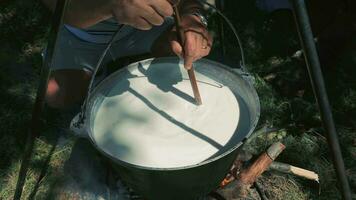 cuisine dans une grand pot en plein air, la personne en remuant avec une en bois cuillère dans une grand pot plus de un ouvert Feu. video